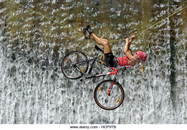 woman-crossing-a-waterfall-on-a-rope-with-a-bike-hcp9tb.jpg